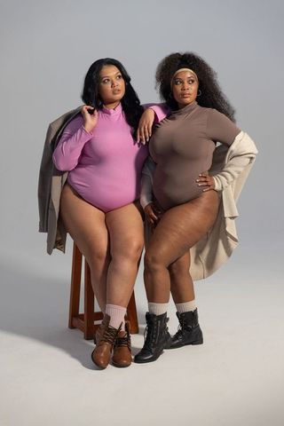 Confident plus size models modeling bodysuits with layered coats and boots in studio