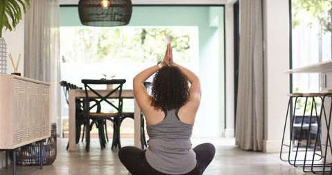 Woman practicing meditation at home on hardwood floor in sunlit open-plan living space