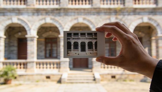 Hand holding polaroid framing historic stone arches in sunlit courtyard