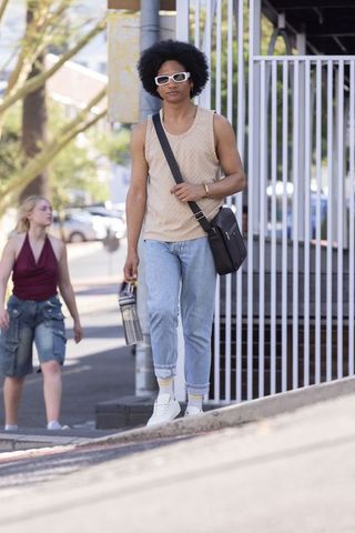 Young man walking uphill with metal water bottle and messenger bag in urban street style