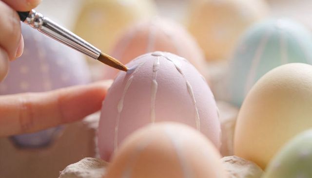Hand painting pastel easter egg with delicate white stripes, close-up diy craft detail