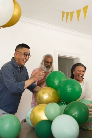 Diverse friends celebrating with green and gold balloons, laughing and clapping indoors