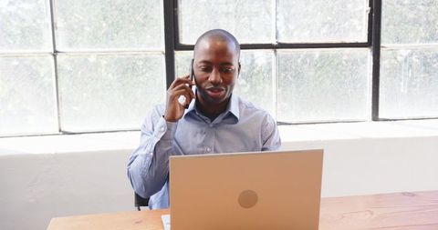 Professional Working on Laptop While Talking on Smartphone in Office