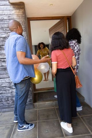 Friends Holding Balloons Greeting Friend in Doorway