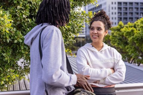 Friends chatting on rooftop terrace wearing hoodies carrying backpack urban cityscape