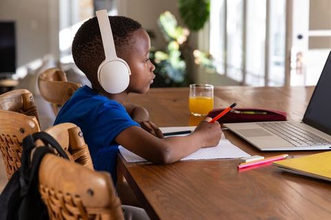 Focused african american boy studying at home with headphones, laptop and notebook