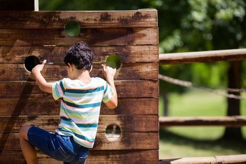 Child Climbing Wooden Wall in Sunlit Adventure Park