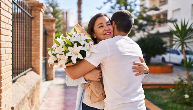 Mother and son hugging with bouquet of white lilies on sunny residential walkway