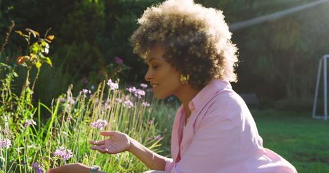 African american woman enjoying garden flowers in warm sunshine