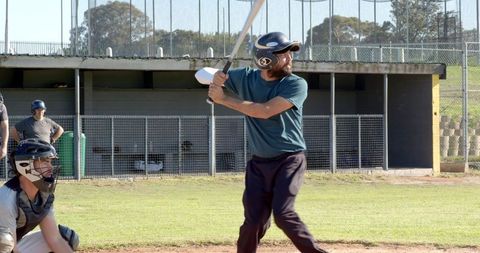 Amateur Baseball Batter Preparing to Swing with Catcher and Teammates Watching Dugout