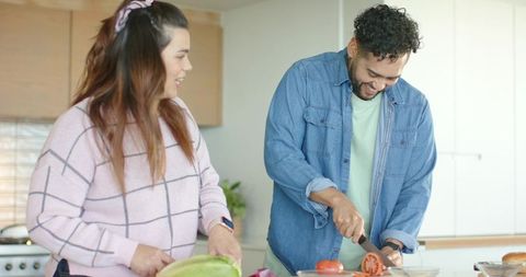 Couple cooking together at bright modern kitchen island, slicing vegetables and smiling
