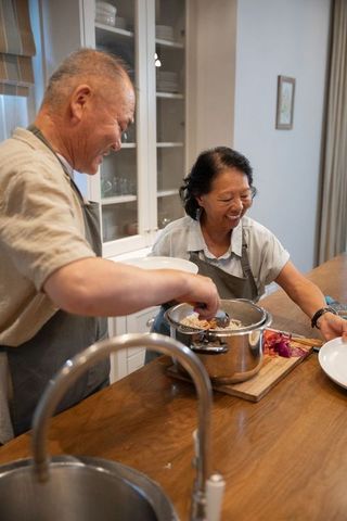 Elderly chinese couple cooking together at kitchen island sharing meal prep and warm laughter
