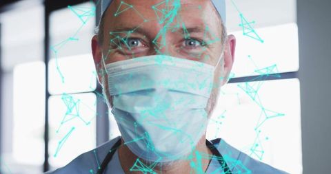 Smiling surgeon wearing surgical cap, mask and scrubs with teal digital network overlay