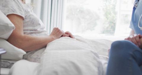Elderly patient receiving compassionate bedside care from nurse in natural daylight