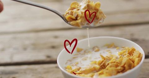 Dripping Milk Over Cornflakes While Lifting Spoon on Rustic Table with Red Heart Doodles