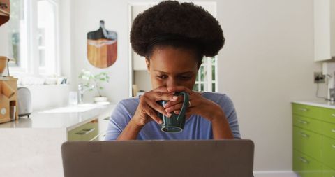 Woman Enjoying Coffee While Using Laptop in Cozy Kitchen