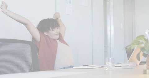 Young woman stretching at meeting table in modern office, relaxing in ergonomic chair
