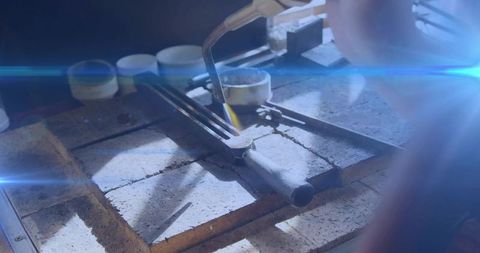 Female jeweler heating crucible with blue torch on firebrick bench for precision casting