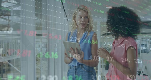 Image of stock market data processing against two diverse women discussing at office. Global economy and business technology concept