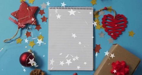 Spiral notepad awaiting holiday gift list on cyan flatlay with festive decorations