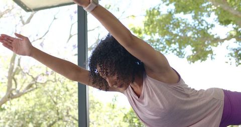 African american woman stretching on patio practicing yoga with smartwatch in activewear