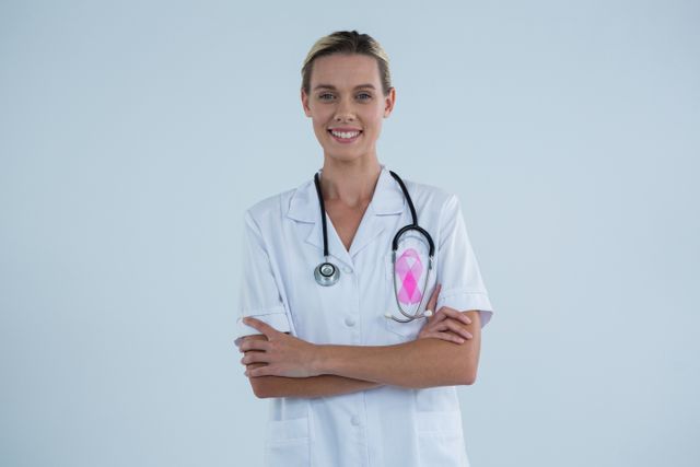 Portrait of female doctor with Breast Cancer Awareness ribbon standing against gray background