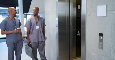 African american male healthcare workers walking and talking by elevator in modern hospital corridor