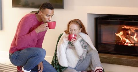 Winter Comfort by Fireplace: Couple Savoring Warm Beverages