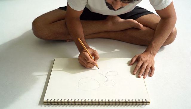 Bearded man drawing geometric sketches sitting cross-legged on pale studio floor