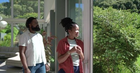African couple standing at open glass door overlooking sunlit garden in minimalist home