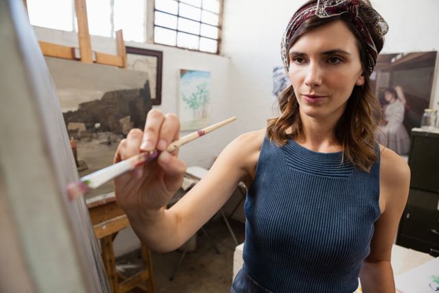 Woman painting on canvas in an art studio, showcasing creativity and concentration. Ideal for use in articles about art classes, creative hobbies, or artistic professions. Suitable for promoting art workshops, painting tutorials, or creative lifestyle content.