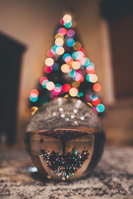 Glass ball reflecting a decorated Christmas tree with colorful bokeh lights in soft focus in background. Perfect for holiday season promotions, festive greetings, lifestyle blogs, Christmas decoration ideas, and warm, cozy winter settings.