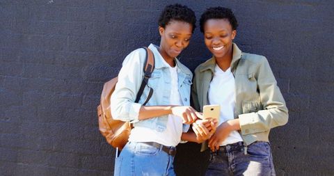 Twin Sisters Sharing Mobile Experience Against Urban Wall