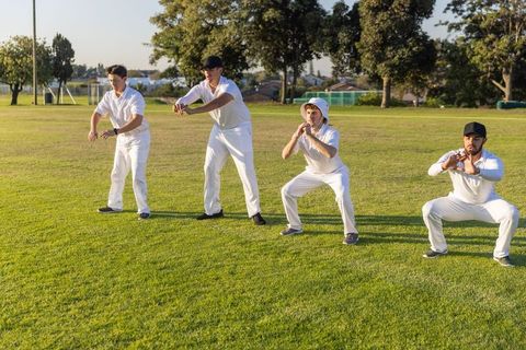 Cricket teammates practicing close fielding drills on sunlit grass pitch at local park
