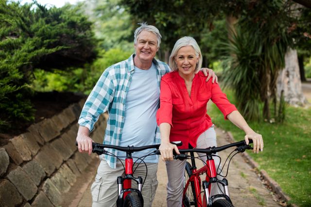 Portrait of senior couple standing with bicycle in park on a sunny day