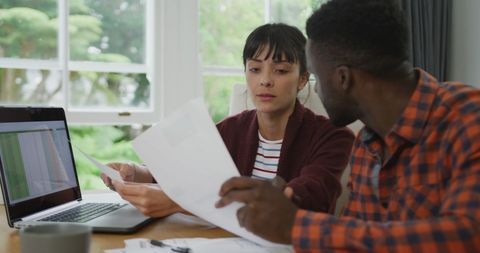 Diverse Couple Collaborating at Home with Laptop and Documents
