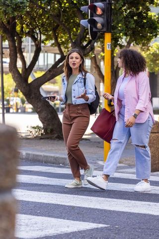 African american friends walking and talking across crosswalk with phones and maroon tote