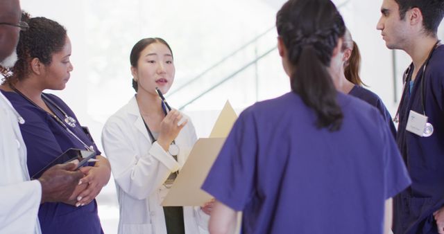 Healthcare professionals dressed in white and blue consult, led by a female doctor holding a pen and a clipboard. Ideal for use in articles, reports, or presentations focusing on medical teamwork, hospital environments, or healthcare consultation.