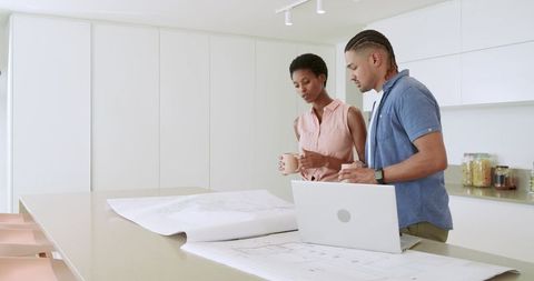 Couple Reviewing Blueprints with Laptop in Modern Kitchen
