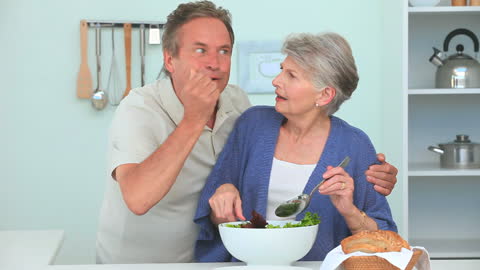 Senior Couple Enjoying a Fun Moment While Making Salad Together in Kitchen