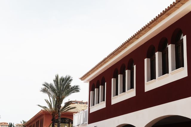 Image captures Mediterranean-style building with arched windows, complemented by palm trees under clear skies. Perfect for travel brochures, vacation marketing, or articles on Mediterranean architecture or destinations.