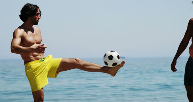 Man enjoying sunny day at the beach casually kicking soccer ball, showcasing leisure and playful summer activity ideal for outdoor apparel, travel promotions, sports gear advertisements, recreational lifestyle features.