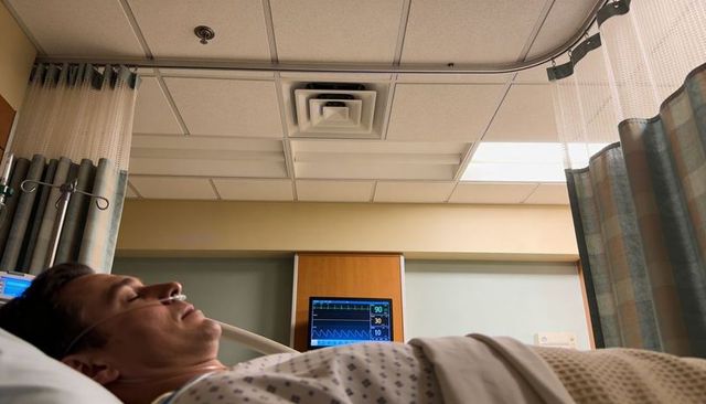 Patient resting on hospital bed receiving oxygen via nasal cannula with vital sign monitor