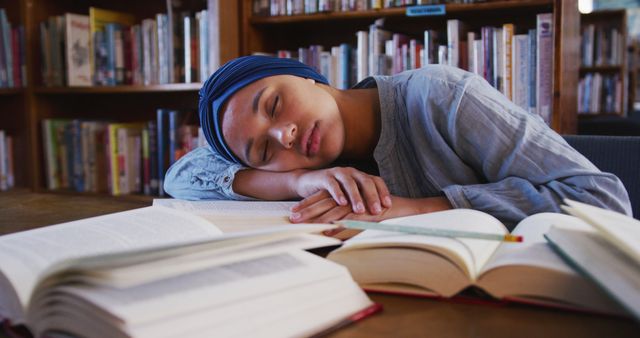 Tired biracial female student sitting and sleeping at desk with books in library. Library, education, studies and feminity, unaltered.