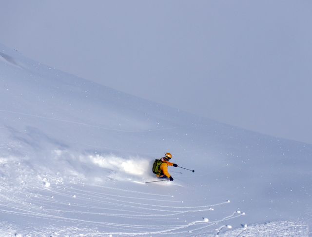 Person skiing downhill on snowy mountain slope with fresh powder. Perfect for advertising winter sports, adventure travel packages, outdoor activity promotions, ski resort marketing, or illustrating articles on skiing techniques and winter holiday destinations.