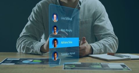 Executive navigating holographic contact list on handheld device with tablet and charts