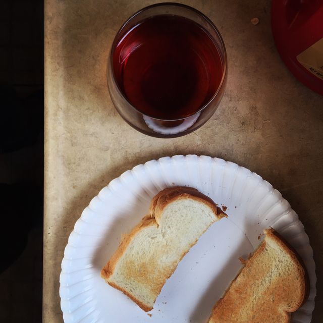 Top view of toast bread cut in half on a white paper plate next to a glass of wine on a white tabletop. This image is ideal for illustrating breakfast, simplicity, casual dining, morning routine, or a relaxed meal setup. Perfect for food blogs, lifestyle articles, or advertisements for breakfast items or beverages.