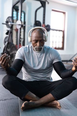 Senior african american man meditating in gym wearing headphones for mindfulness wellness