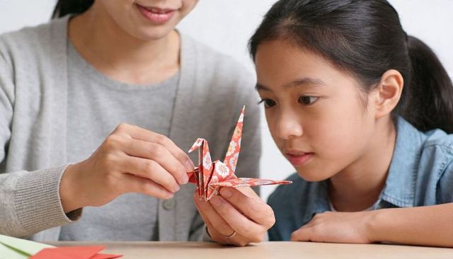 Mother teaching daughter folding decorative origami crane, family crafting moment