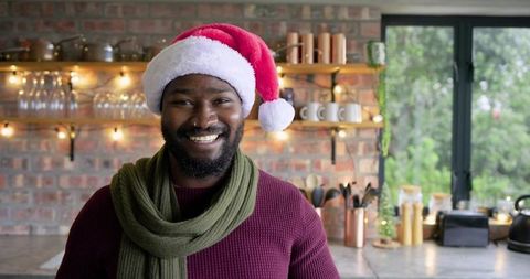 Smiling African American man wearing Santa hat and green scarf in cozy kitchen